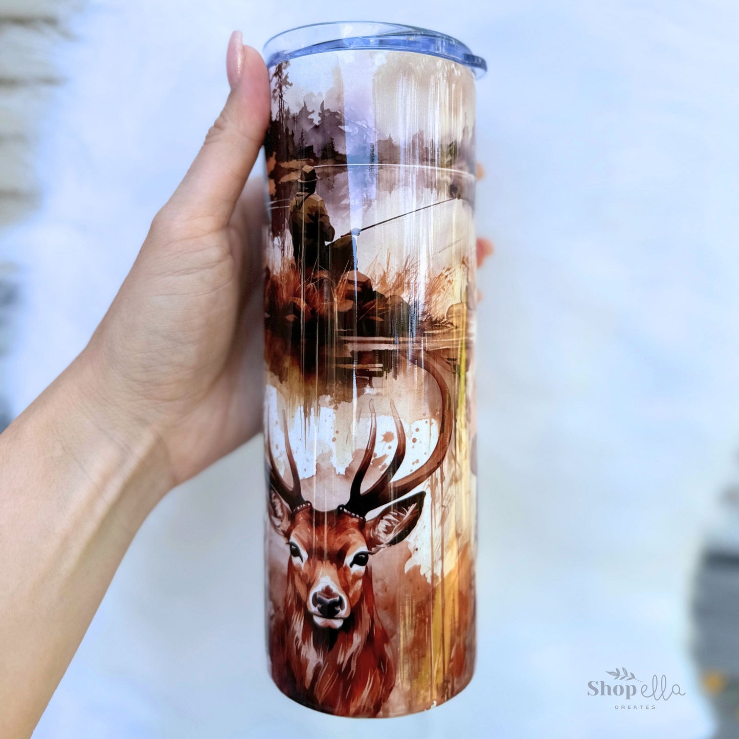 a hand holding a white 20oz skinny tumbler with lid with hunting and fishing images for men