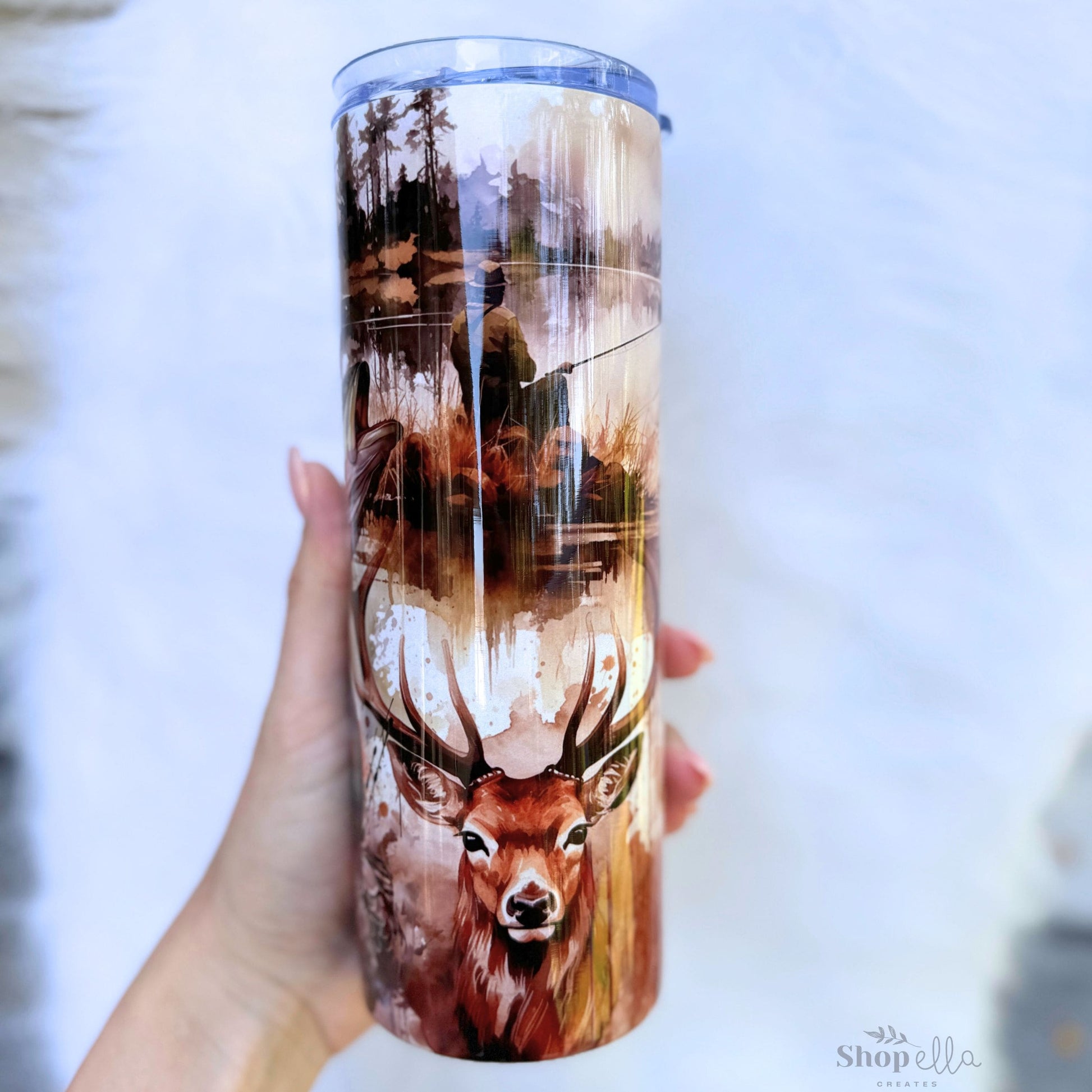 a hand holding a white 20oz skinny tumbler with lid with hunting and fishing images for men