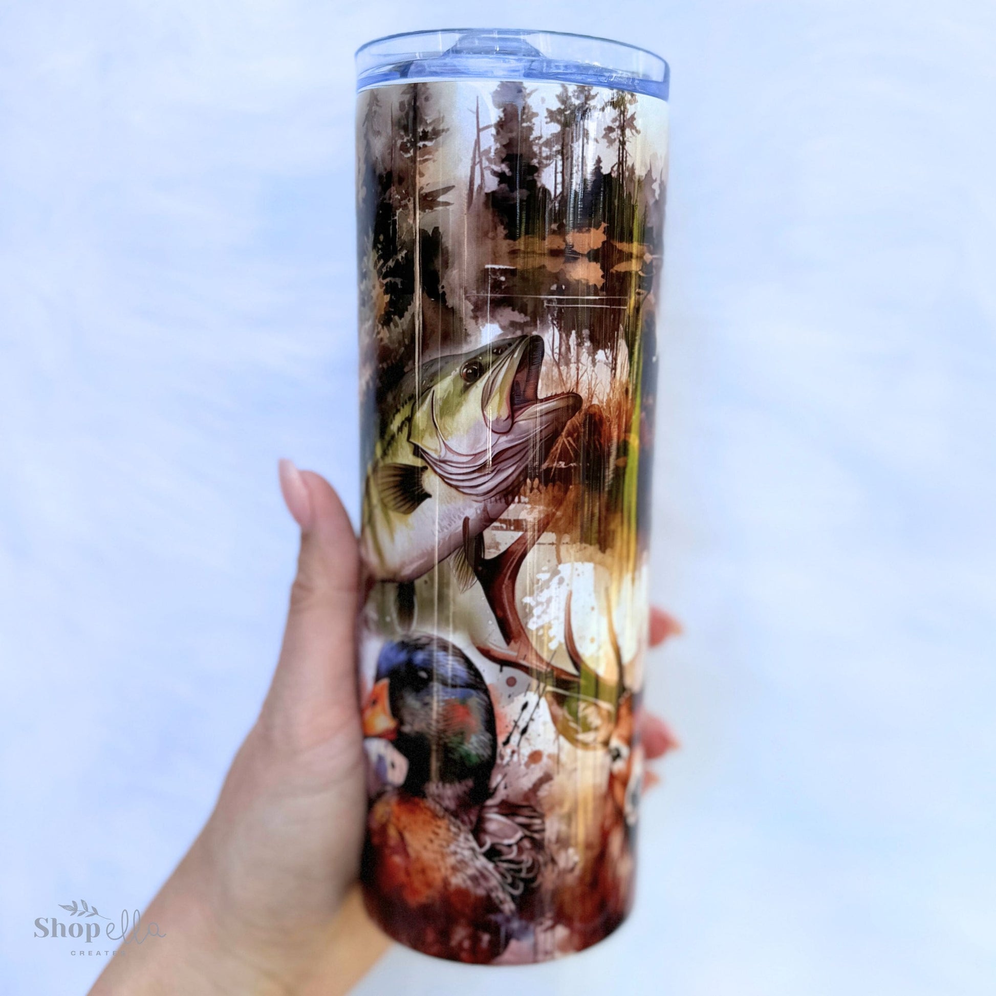 a hand holding a white 20oz skinny tumbler with lid with hunting and fishing images for men