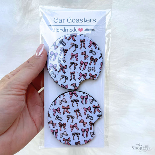 a hand holding a package of car coasters coquette bows pink and beige on white background